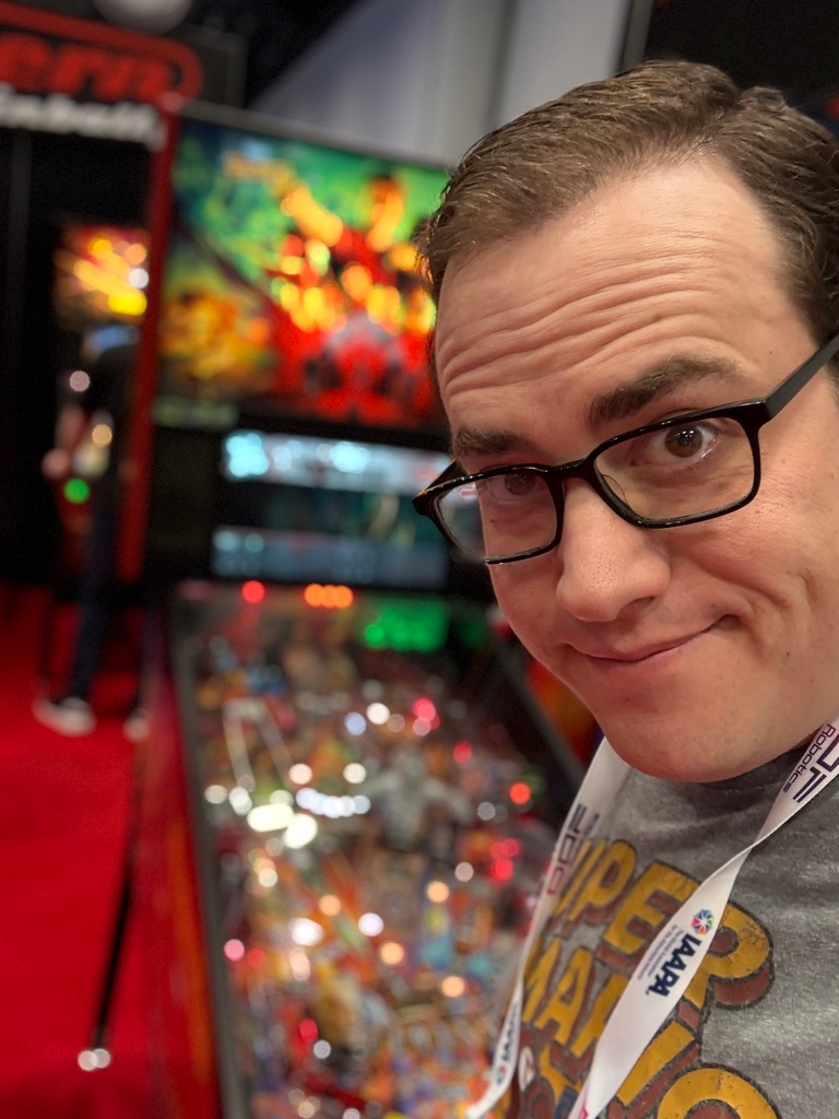 Scott Green grinning beside a pinball machine at a pinball expo