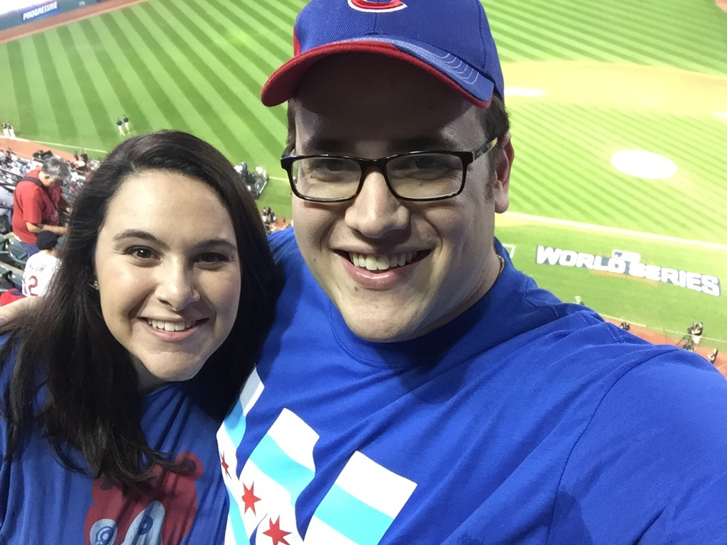 Scott Green and his wife smiling in Cubs shirts, the World Series field behind them