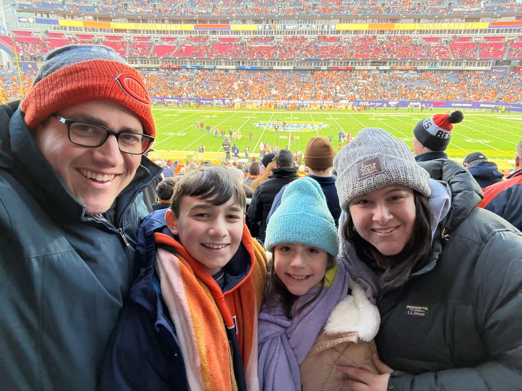 Scott Green, his wife and their two children in winter hats, smiling in the stands at a football bowl game
