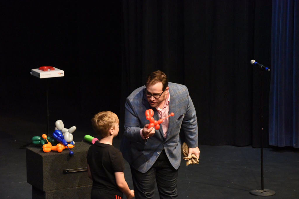 Scott Green handing a balloon dog to a young volunteer on stage