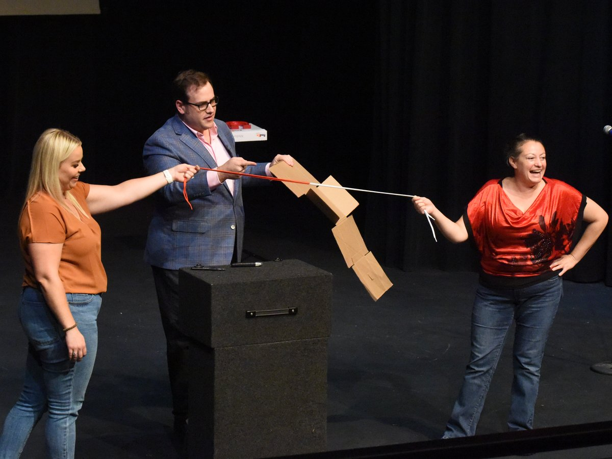 Scott Green with two volunteers and a suspended cardboard effect on stage in Sedalia, Missouri